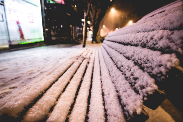 panchina in legno nella strada di una città ricoperta di neve che è caduta in inverno - Foto, immagini