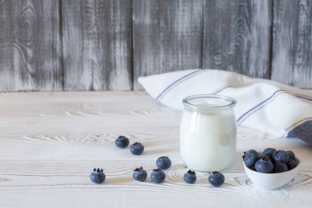 A healthy breakfast of Greek yogurt in a glass jar and fresh blueberries at a rustic white table. Selective focus on glass jar in front with blurred background - Photo, Image
