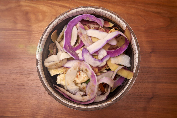 Turnip doméstico e cascas de aipo em uma panela de cerâmica em uma mesa de madeira áspera à espera de ser jogado na lixeira do composto - Foto, Imagem