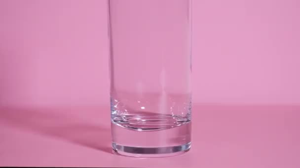 Наливаємо воду в прозоре скло на рожевий фон. Ефективна таблетка потрапляє в склянку води
. - Кадри, відео