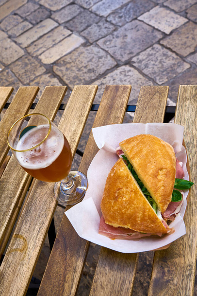 Ιταλικό σάντουιτς με στεγνό ζαμπόν με σαλάτα από μαρούλι αρνιού σε ξύλινο τραπέζι με ποτήρι μπύρα - Φωτογραφία, εικόνα
