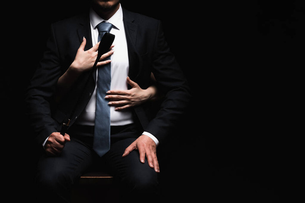 a női karok ölelkeznek egy férfi domináns öltönyben egy bőrostorral Flogger. A BDSM szex fogalma - Fotó, kép