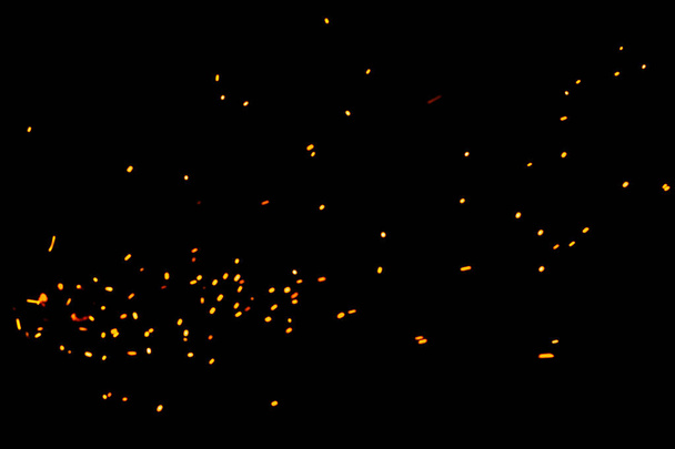 Faíscas naturais amarelo-quentes de fogo em um fundo preto, bokeh amarelo brilhante do fogo. Partículas de brasas ardentes voam e brilham isoladas no céu noturno. - Foto, Imagem