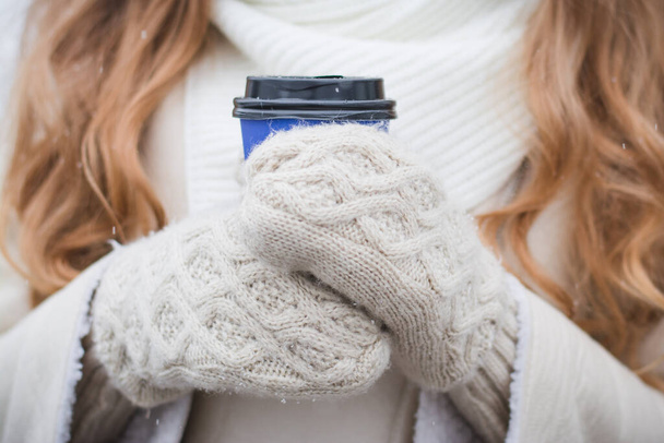 Woman warming up hands in grey woolen gloves and cup of coffee or tea in winter - Fotó, kép