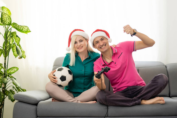 νεαρό ζευγάρι παίζει βιντεοπαιχνίδι με joysticks στο σπίτι για τα Χριστούγεννα - Φωτογραφία, εικόνα