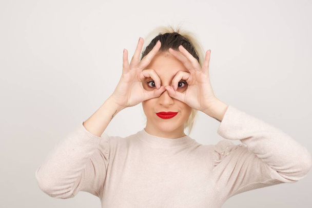 Игривая, возбужденная женщина показывает жест ОК обеими руками, притворяясь, что носит очки - Фото, изображение