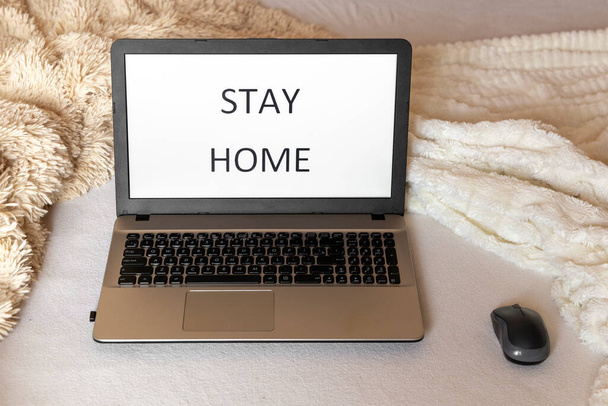 Notebook na posteli s nápisem "zůstaň doma" na obrazovce. Útulný koncept domova. Práce z domova - Fotografie, Obrázek