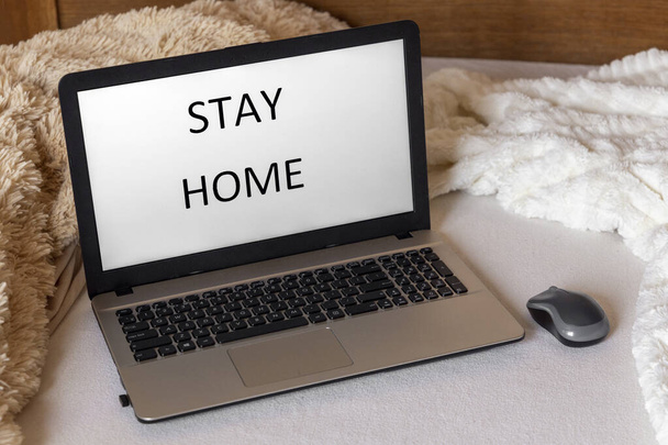 Notebook na posteli s nápisem "zůstaň doma" na obrazovce. Útulný koncept domova. Práce z domova - Fotografie, Obrázek