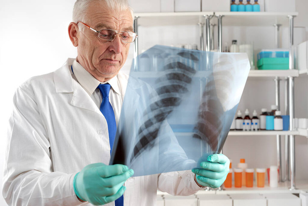 Tohtori vanhempi mies valkoisessa takissa tutkii röntgenkuvaa sairaalassa. - Valokuva, kuva