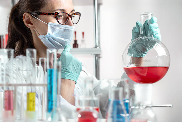 assistente di laboratorio di chimica donna guardando liquido colorato in vetro di laboratorio. - Foto, immagini