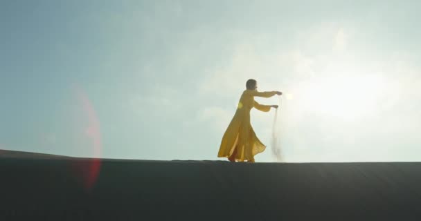 Mujer con estilo en vestido amarillo caminando sobre la duna de arena en cámara lenta - Metraje, vídeo