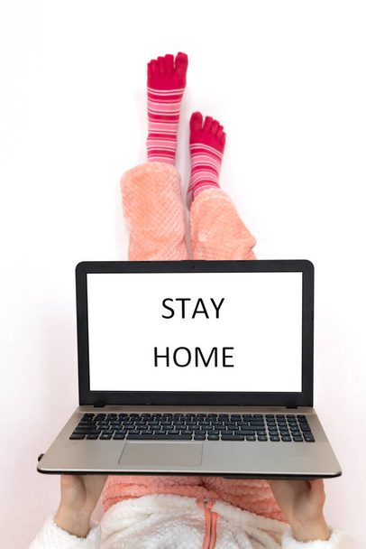 Stay home written on laptop screen. Legs up in pink socks on the white background - Fotografie, Obrázek