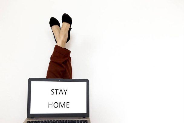 Woman in office clothes holding laptop with "Stay home" text and copyspace. Quarantine and isolation concept. Legs up, remote work from home, remote job - Fotografie, Obrázek