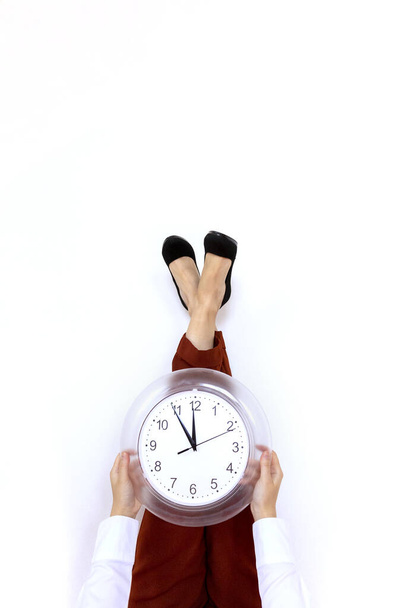 Legs in office suit and high heels up on the wall and holding office clock in hands with white background. Time management and job schedule concept. - Zdjęcie, obraz