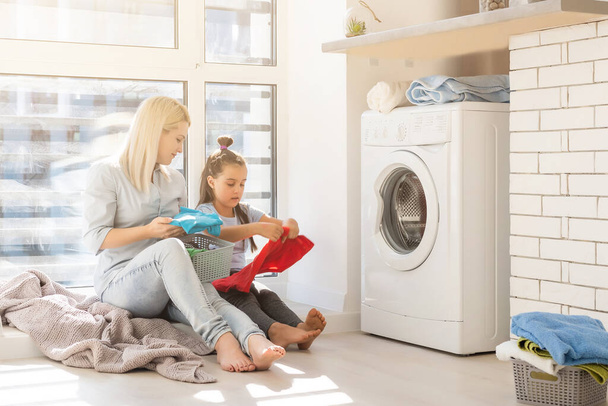 Mutlu ev hanımı ve kızı çamaşır makinesinin yanında çarşaf taşıyor. - Fotoğraf, Görsel