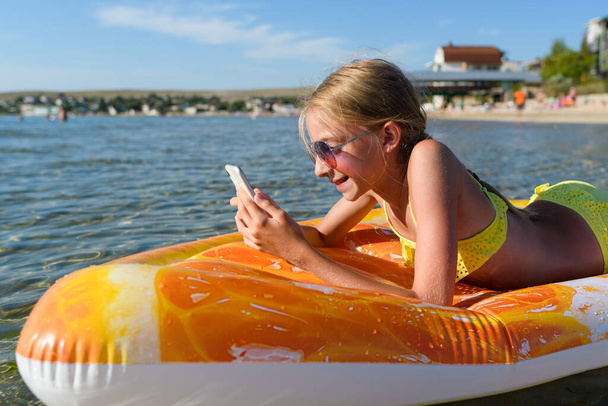 Das Mädchen schwimmt auf einer aufblasbaren Matratze im Meer und spielt mit einem Smartphone. Das Mädchen am Meer telefoniert. - Foto, Bild