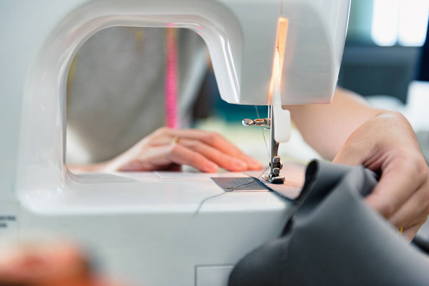 Primer plano Prensatelas de máquina de coser, Mano de mujer joven modista trabajando con una máquina de coser en su estudio de corte. Punto de enfoque muy superficial en el prensatelas - Foto, Imagen
