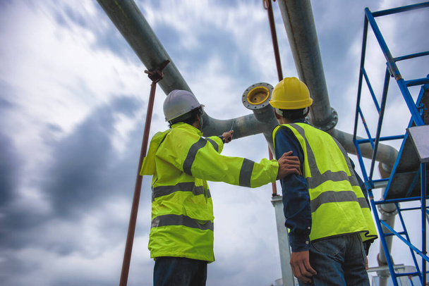 Dos ingenieros con chaleco reflectante de seguridad de malla amarilla discutido en el sitio de construcción y señalando el trabajo. - Foto, Imagen