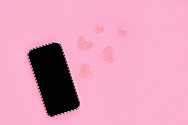 ピンクの背景に心を感じた黒画面で携帯電話をモックアップします。コピースペース。オンライン会話、誕生日やバレンタインデー. - 写真・画像