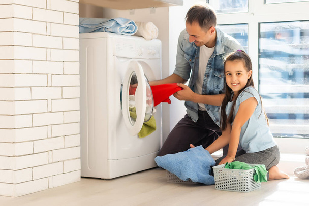 Счастливая семья мужчина отец домовладелец и дочь в прачечной со стиральной машиной - Фото, изображение