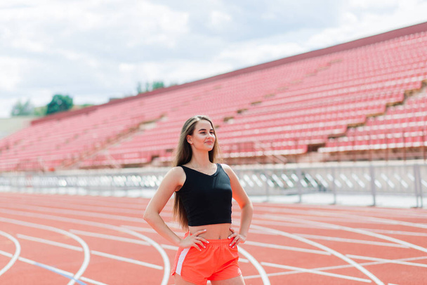 Молодая, красивая спортсменка в спортивной одежде тренируется и бегает, растягиваясь на стадионе - Фото, изображение