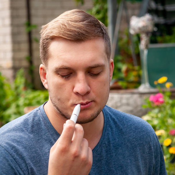 Портрет небритого мужчины, отдыхающего в городском парке. Курить сигарету - Фото, изображение
