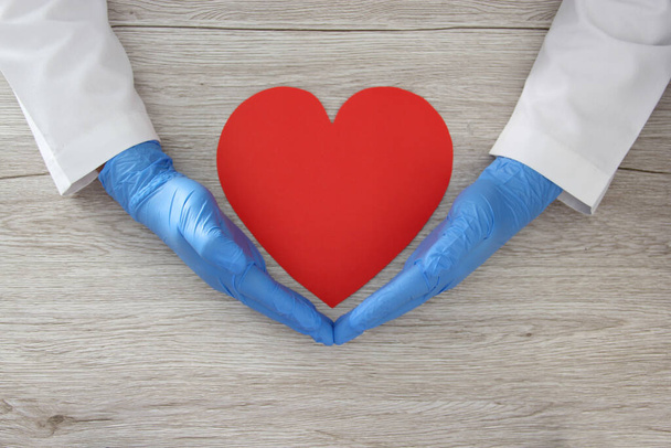 Την ημέρα του Αγίου Βαλεντίνου. καρδιά στα χέρια του γιατρού με λατέξ και γυναικεία γάντια, vintage ξύλινο υπόβαθρο για τη διαφήμιση baner - Φωτογραφία, εικόνα
