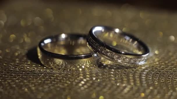 Svatební kroužky ležící, rotující, rotující na lesklém zlatém lesklém povrchu s lehkým, detailním makro - Záběry, video