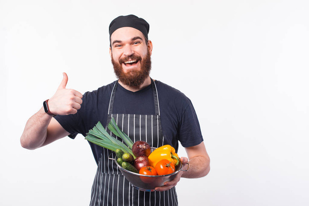 Foto van een vrolijke bebaarde chef-kok in uniform met groenten in schaal - Foto, afbeelding