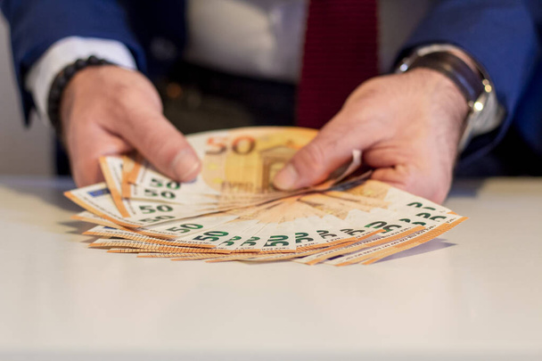 Uomo d'affari che mostra in mano cinquanta banconote in euro. Concetto di risparmio finanziario e monetario - Foto, immagini