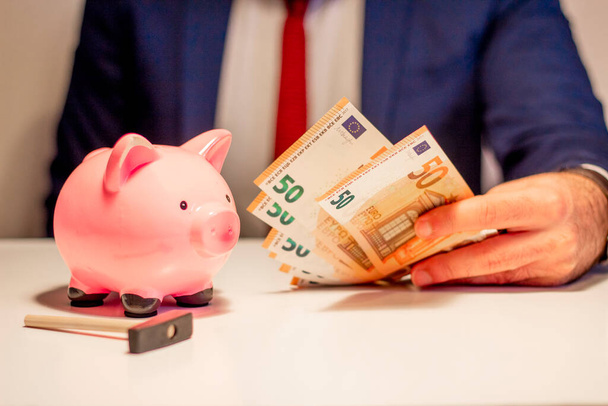 Zakenman met vijftig eurobiljetten, spaarvarken en hamer in close-up. Financieel en geldbesparingsconcept - Foto, afbeelding