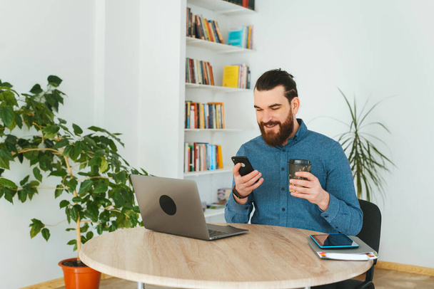 Щасливий офісний працівник використовує смартфон і тримає чашку кави
 - Фото, зображення