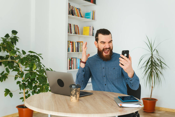 Photo of angry man in office screaming at smartphone - Photo, Image