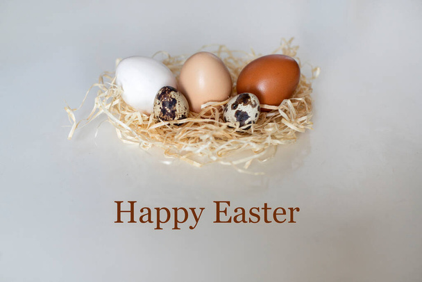 Tarjeta de Pascua con la inscripción Feliz Pascua, y huevos de codorniz y pollo en un nido de mimbre - Foto, Imagen