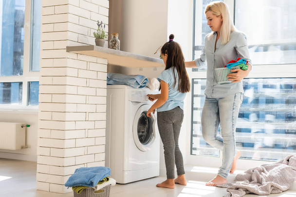 Молода домогосподарка і маленька дівчинка роблять прання разом
 - Фото, зображення