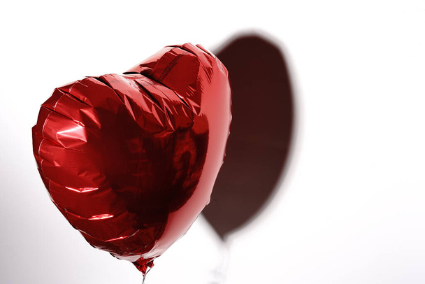 Un corazón inflado con helio vuela sobre una cuerda sobre un fondo blanco. Un regalo para el Día de San Valentín. - Foto, imagen