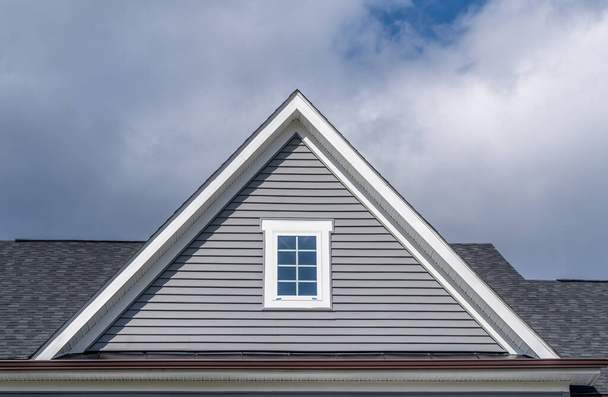 Gable with grey horizontal vinyl lap siding, double hung window with white frame, vinyl shutters on a pitched roof attic at a luxury American single family home neighborhood USA - Fotó, kép
