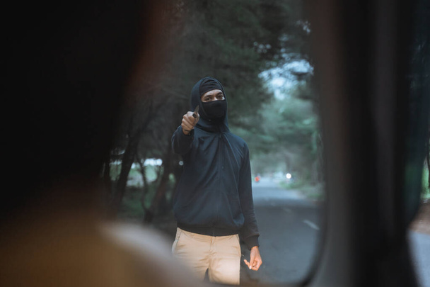hombre con una máscara utiliza un cuchillo para amenazar al conductor del coche - Foto, imagen