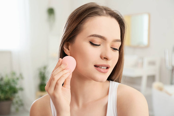 Beautiful young woman with sponge applying makeup at home - Photo, Image