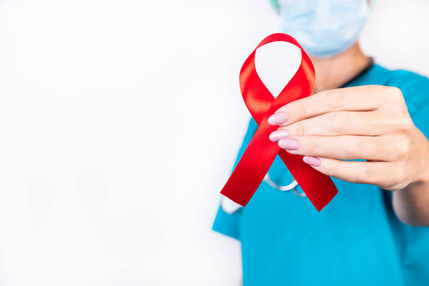 Red ribbon in a doctor's hand as a symbol of help awareness on a white background. - Foto, immagini