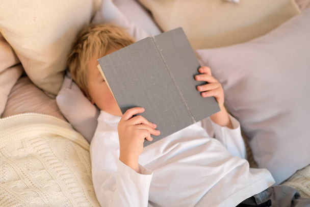 happy boy read book. little boy holding a book in his hands, concept of reading in bed - Foto, Imagem