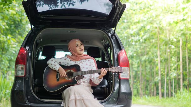 mujer asiática tavelling usando hijab jugando guitarra con un coche  - Foto, imagen