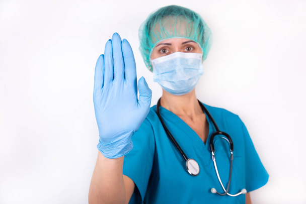 Young beautiful female doctor makes a stop gesture with the palm of his hand. Warning expression with a negative and serious gesture on his face isolated on a white background. - Foto, Imagen