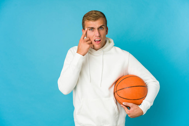 Junge kaukasische Mann beim Basketballspielen isoliert auf blauem Hintergrund schockiert, sie erinnert sich an wichtiges Treffen. - Foto, Bild