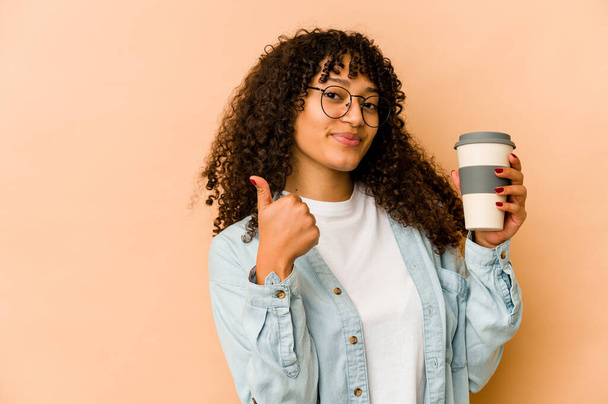 Young african american afro woman holding a takeaway coffee smiling and raising thumb up - Photo, Image
