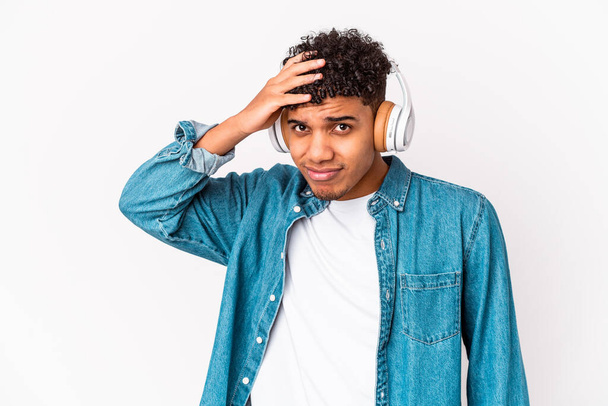 Jovem homem encaracolado afro-americano isolado ouvindo música com fones de ouvido sendo chocado, ela se lembrou de reunião importante. - Foto, Imagem