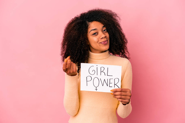 Young african american curly woman holding a girl power message on a placard pointing with finger at you as if inviting come closer. - Foto, afbeelding