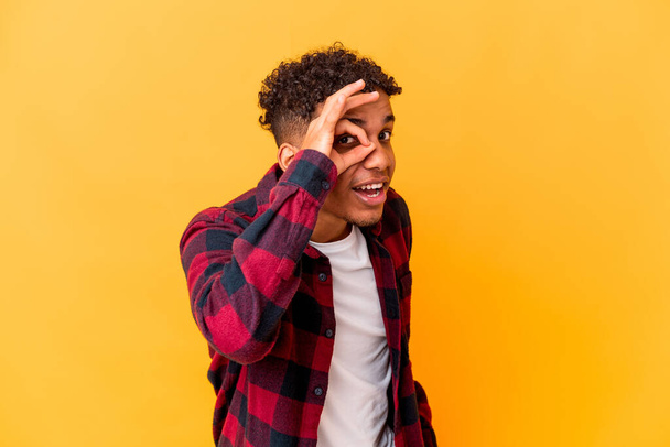 Молодий афроамериканський кучерявий чоловік ізольований на фіолетовому збудженому тримає очний жест на очах
. - Фото, зображення