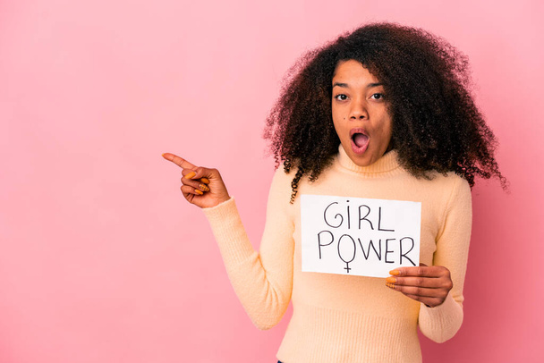 Νεαρή Αφροαμερικάνα σγουρή γυναίκα που κρατά ένα μήνυμα κοριτσίστικης δύναμης σε μια πινακίδα που δείχνει το πλάι. - Φωτογραφία, εικόνα