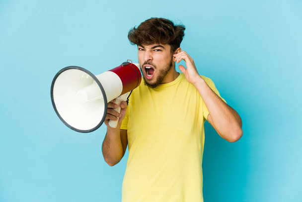 Young arab man holding a megaphone covering ears with hands. - Φωτογραφία, εικόνα